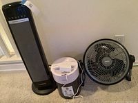 Photo showing the Lasko tower heater, HoMedics humidifier, and Geek Aire fan positioned next to each other on carpet with wall outlet.