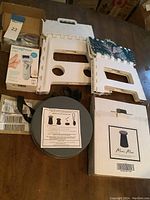 Photo showing Micro Pedi box, accessories in a cardboard box, 2 white plastic folding stools and Mini Max gray round folding stool with strap.