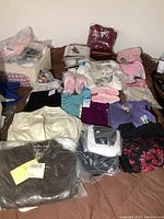 Overview of all clothing items including slippers, robes, tops, and bags, most packaged and new.