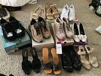 Full view of 11 pairs of ladies shoes arranged on floor showing variety of styles including athletic, casual, heels, slides, and flats in mostly neutral colors, size 7.