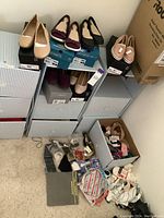 Stack of shoeboxes with six pairs of ladies size 7 shoes on top and in shelves, plus a box containing scarves, jewelry, and socks on the floor.