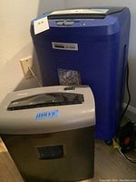 Two paper shredders together, blue Embassy LFT 200 and silver-black Shredsafe WM845XE with dimension labels
