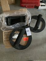 Photo showing black metal circular weight plates with padded grips and a box containing The Block dumbbell set.