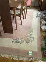 Full view of the corner of the pink and cream floral design rug under a dining table, showing the fringe and floral pattern.