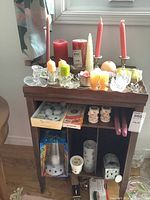 Wide view of all items arranged on a wooden shelf including candles, holders, lantern, and matches.