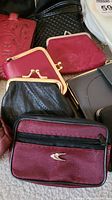Photo showing a variety of women's coin purses and small wallets in red, maroon, black and gray fabric and vinyl materials. Several have metal clasp or zipper closures.