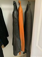 Side view of three coats hanging on a rack: dark black leather coat, brown leather coat, and dark gray fabric coat.
