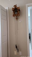 Full view of vintage wood cuckoo clock hanging on wall, showing chains and pinecone weights.