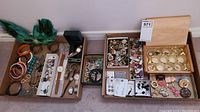 Wide view of entire lot on floor showing boxes of bracelets, watches, rings, brooches, earrings and a feather mask