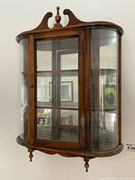 Front angled view of Butler curio cabinet showing curved ends, glass door, and finial on top.