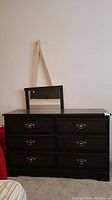 Front view of dark brown wood dresser with six drawers and attached rectangular mirror.
