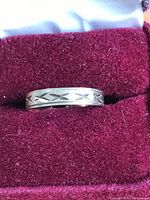 Photo showing the gold band placed inside a red velvet ring box, highlighting the etched geometric pattern around the band.