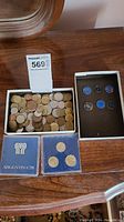 Photo showing a box filled with a large number of assorted loose coins, two blue Argentina 78 coin cases with coins inside and foam protective holders.