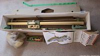 Wooden case open showing full hand knitting machine, accessories, instruction manual