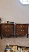 Two wooden nightstands placed side by side with several decorative items on top and a box of jewelry in front.