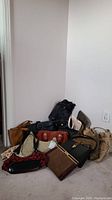 Overview photo showing eleven assorted purses arranged on floor against corner wall, various styles and colors in canvas and vinyl materials.