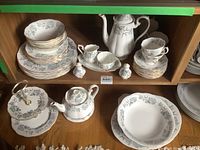 Full set displayed inside wooden shelf showing teapot, cups, saucers, cream and sugar, salt and pepper, coffee pot with 2-tiered tray and small serving tray.