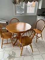 Photo showing round wooden dining table with three chairs around it near a window.