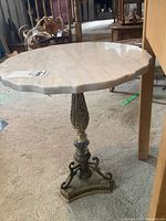 Full view of the table showing the round white marble top with scalloped edges and ornate metal base.