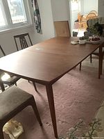 Wide shot of the rectangular solid wood dining table with tapered legs, showing the surface and part of the leaf extension.