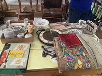 Table display of various porcelain items including small plates, cups, and cake stand, along with a vintage wall clock, boxed papers, and Mexican bark painting.