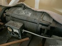 Side view of the metal cylindrical generator housing showing worn label plate and attached control box with gauge and dial.