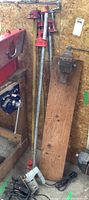 Four bar clamps standing against wall near clamping vice mounted on wood plank