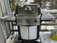 Full front view of stainless steel Broil King Signet grill on snow-covered deck with side shelves and closed cabinet doors