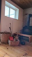 Overall view showing wood bench, wicker baskets of various sizes, fireplace tools, and wood stove nearby
