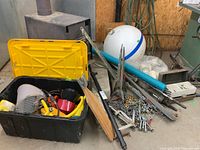 Wide view of black and yellow storage tote, marker buoy, pool noodle, oar, anchors, chains and fishing poles on garage floor