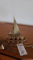 Solid brass sailboat figurine with base and four heart-shaped hooks on an oval rack, displayed on wood surface