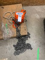 Full view of chain hoist on wooden bench showing orange housing, load chain and braided pull rope.