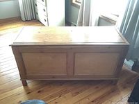 Front view of rectangular solid wood storage chest showing hinged lid and paneled sides.