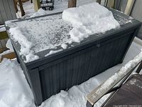 Full view of outdoor gray plastic deck box covered partially with snow, showing overall size and condition.