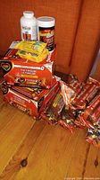 Overview image showing two cases of ZIP firelogs stacked, seven loose firelogs in orange packaging, two containers of chimney cleaner (Imperial Sweep and Tight Stuff), and three yellow packages of Firestarter firelighters on top of a wooden floor with orange curtain background.