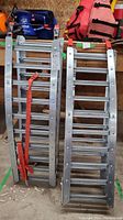 Two Prime brand metal loading ramps standing vertically against a wood wall, with visible red safety straps and metal rung treads.