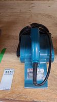 Front angled view of blue Makita power planer with electric cord coiled on top, placed on wood surface with lot tag.