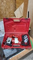 Open red plastic Milwaukee case showing electric jig saw inside with power cord and accessories.