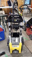 Front view of Karcher pressure washer showing hose coiled on front, handle, wheels, and connection fittings