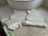 Two white sheepskin rugs laid on carpeted floor in front of white trimmed bathtub