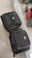 Front view of two black Harley Davidson saddlebags with logo, zippers, and handles visible.