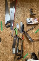 Overview photo of all saws and tools including handsaws, hacksaws, coping saw, backsaw, saw guide, and sharpening tool on wood board
