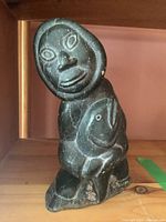 Front view showing facial features, hood and fish held in arms.