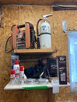 Overview shelf photo featuring Black & Decker jump starter, fire extinguisher, propane tanks, butane fuel canisters, respirator mask, air filter cartridges, and 12 volt air compressor partially visible.