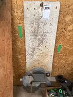 Wide view of the heavy metal bench vice mounted on a tall wooden board, showing its size and condition.