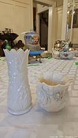 Both Belleek vases shown together on a table among other antiques and ceramics