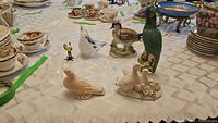 Full view of six bird figurines varying in sizes and colors arranged on a table with china cups in background