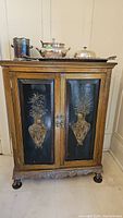Front view of antique cabinet showing two doors with decorative carved panels and five drawers below.