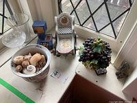 Wide view showing porcelain carriage, ceramic grapes sculpture, blue ceramic statue, vase with sea shells, glass vase, and crystal glass near window