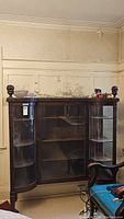 Front full view of the vintage wooden display cabinet showing ornate woodwork, glass front doors, and items on top.